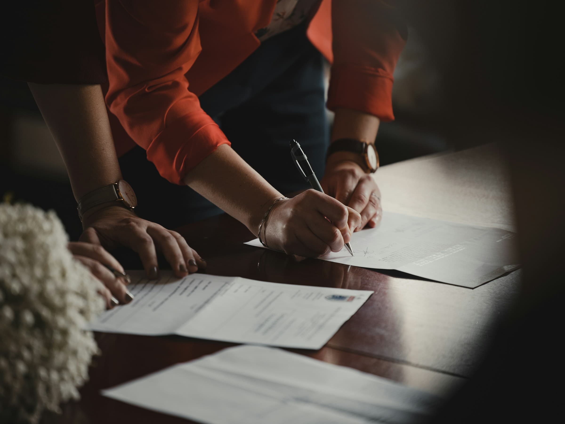 A woman signing a document at a table, witnessed by another person.